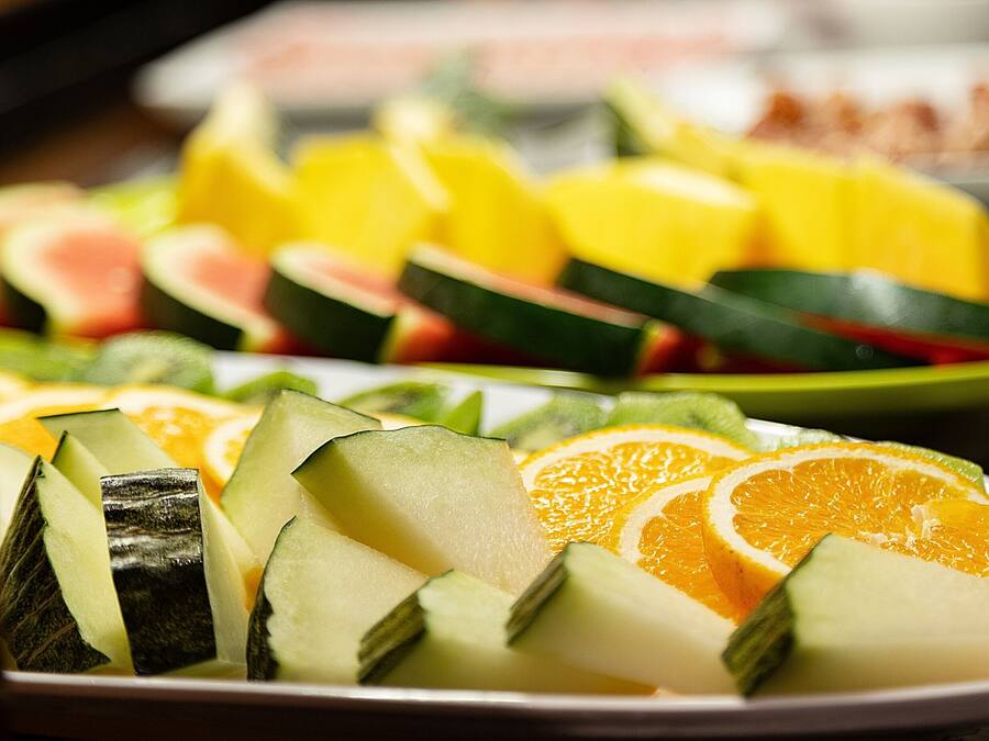 Lautaselle on aseteltu erilaisia tuoreita hedelmiä, kuten vesimelonia, appelsiinia ja kurkkua viipaleina.