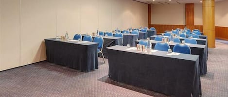 A conference room with multiple tables and chairs, carpeted floor, and a large pillar.