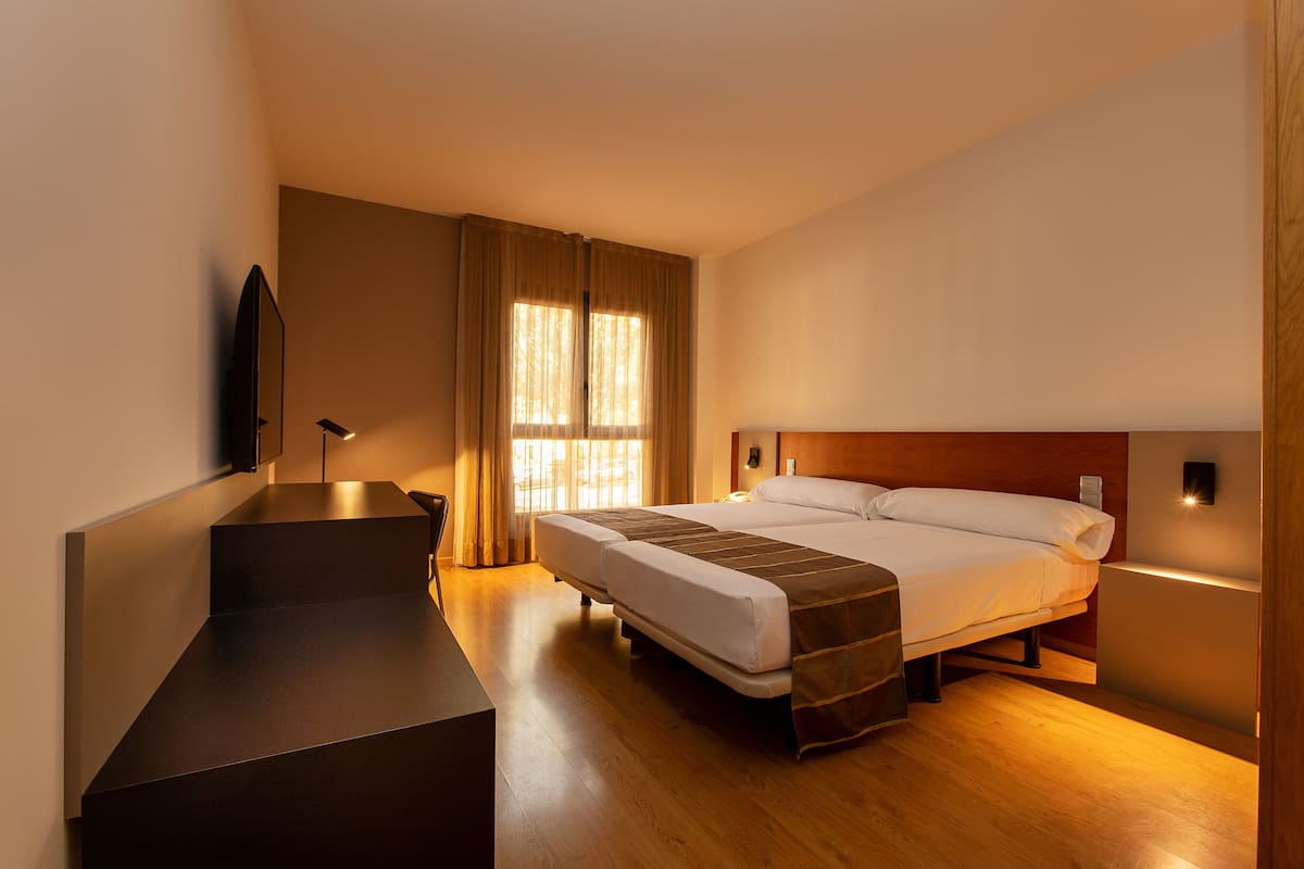 A modern hotel room with a large bed, a desk, and a view of the outdoors through the window.