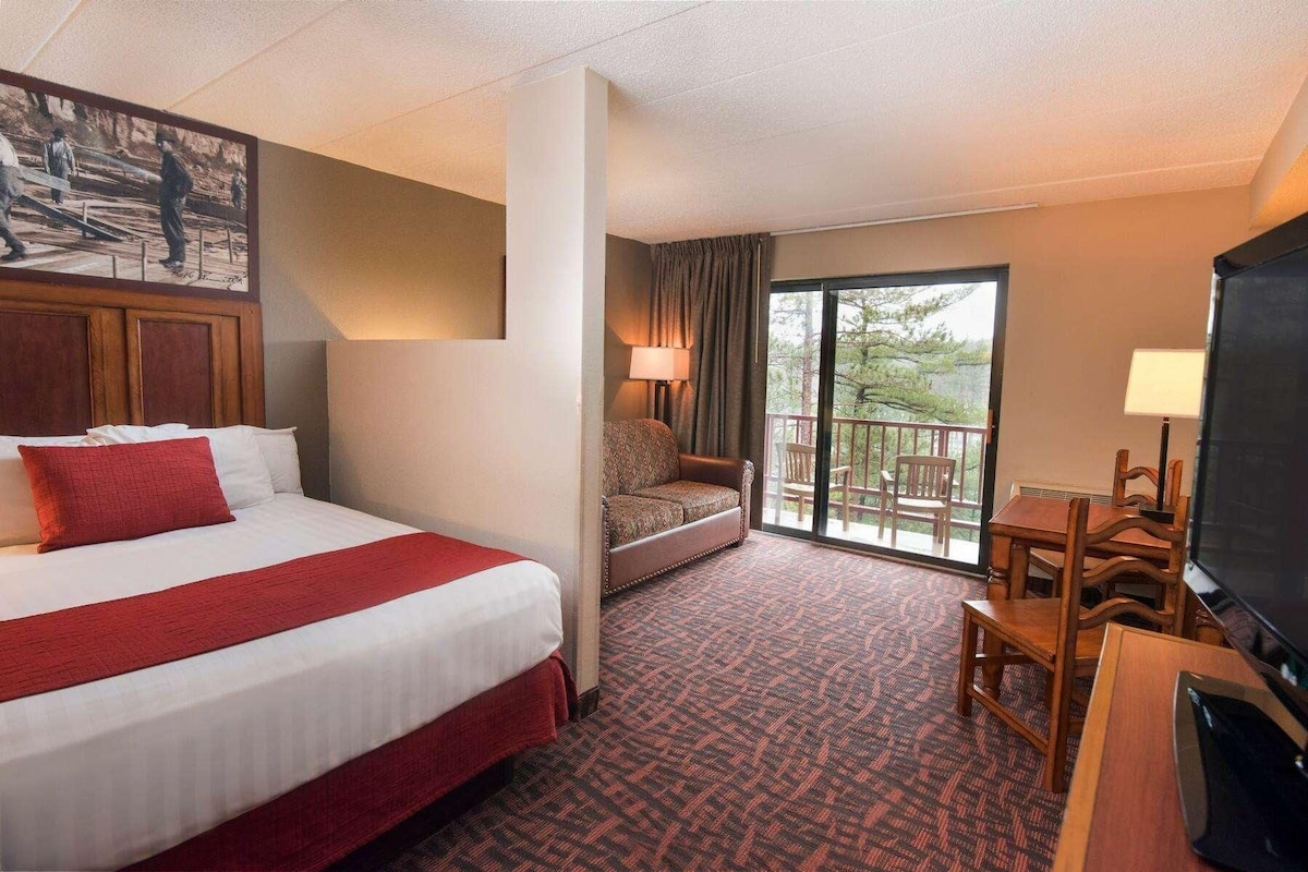 A hotel room with a large bed, a sofa, a balcony with a view, and a TV.