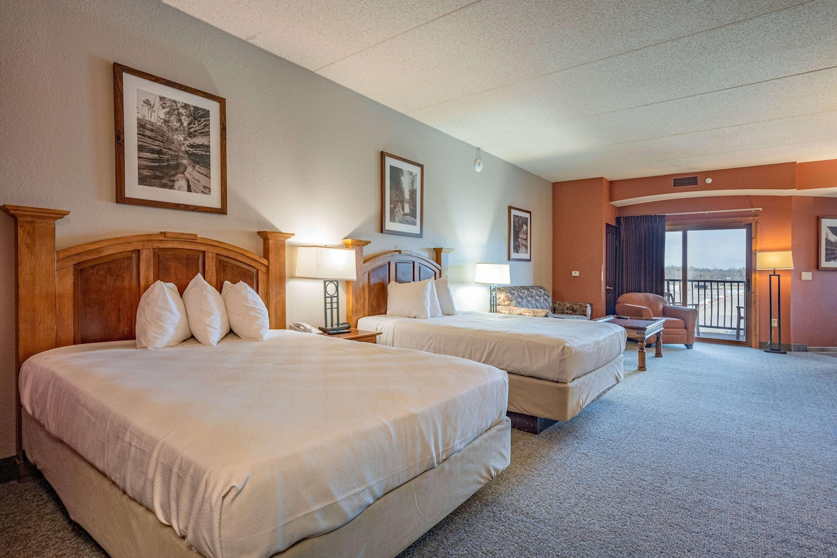 A hotel room with two beds, a desk, a chair, and a balcony with a view.
