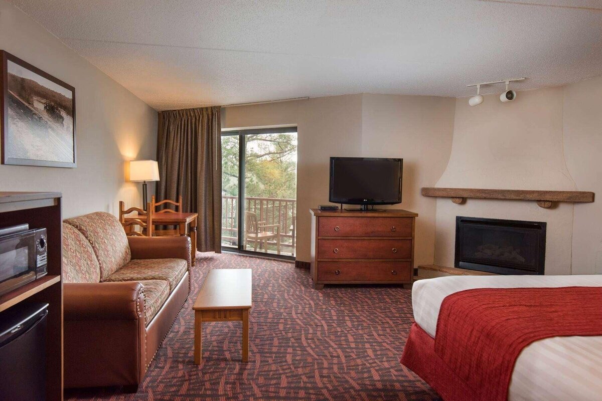 A hotel room with a sofa, a small table, a television, a fireplace, and a balcony with curtains.