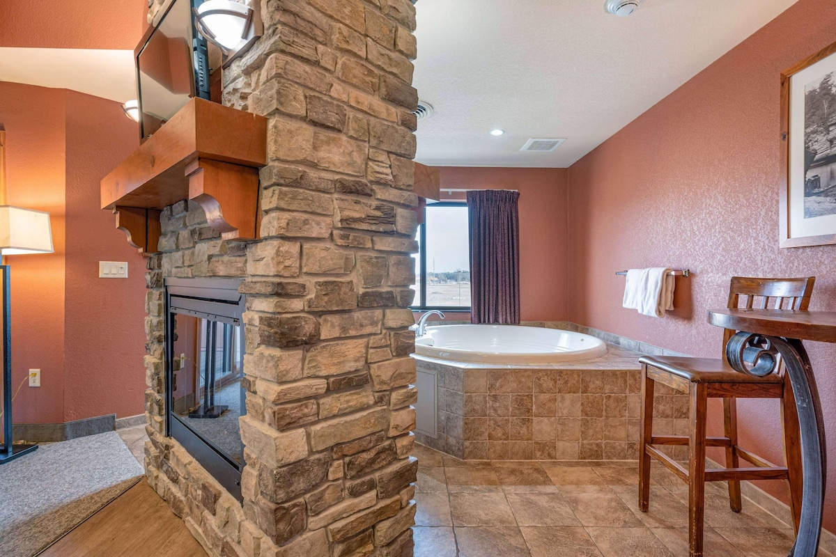 A bathroom with a stone wall, a bathtub, a wooden chair, and a window with curtains.