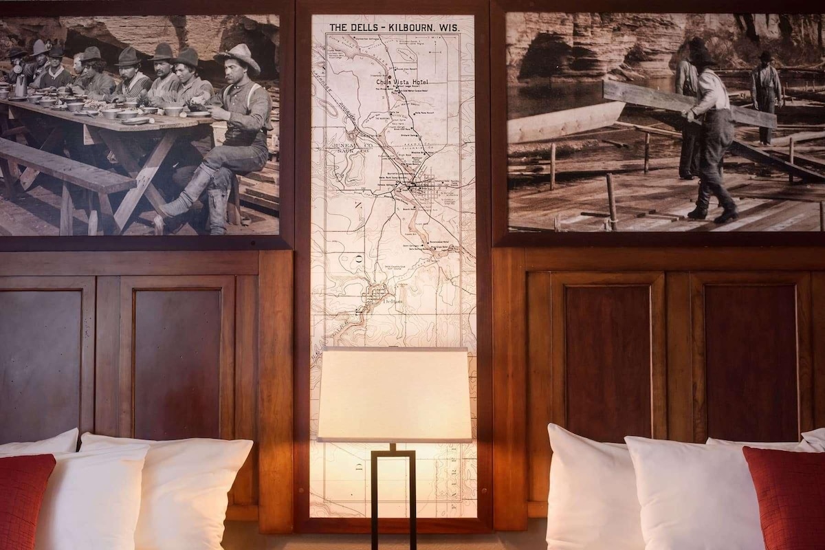 A room with wooden paneling, a large map on the wall, and a bed with pillows.
