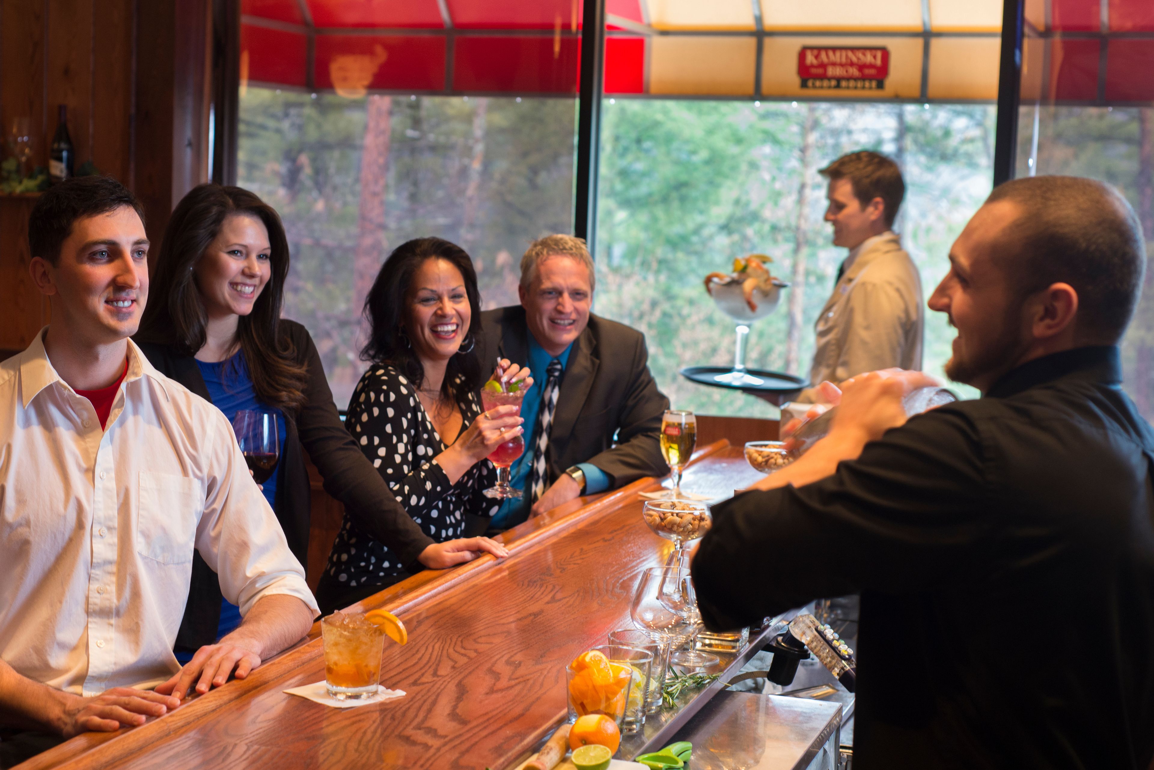 A group of people seated at a bar with a view of trees outside.