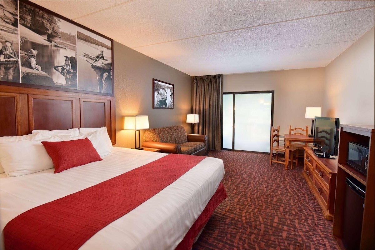 A hotel room with a large bed, two bedside lamps, a television, a desk with a chair, and a door leading to a balcony.