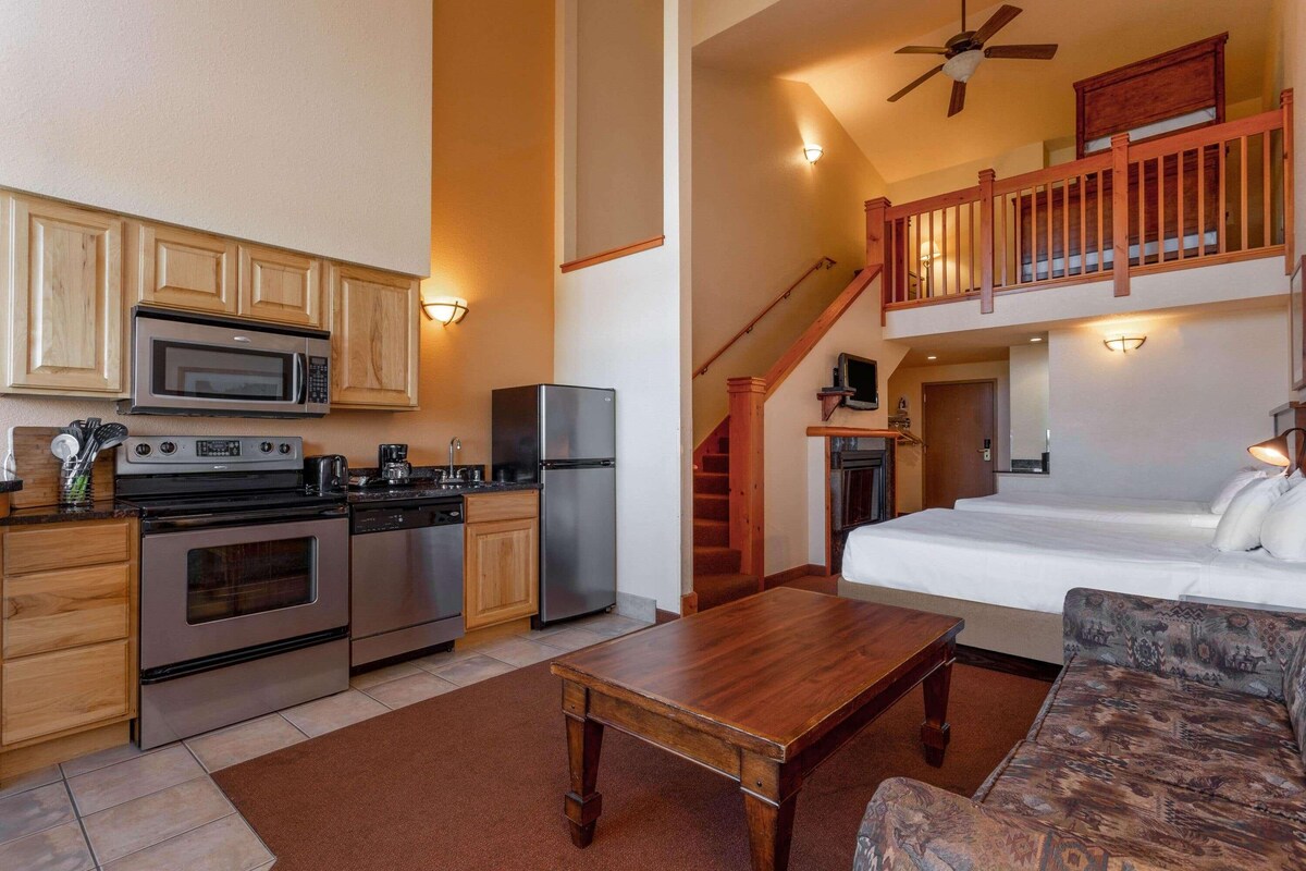 A compact living space with a kitchenette, a dining area, a sofa, and a staircase leading to an upper level.