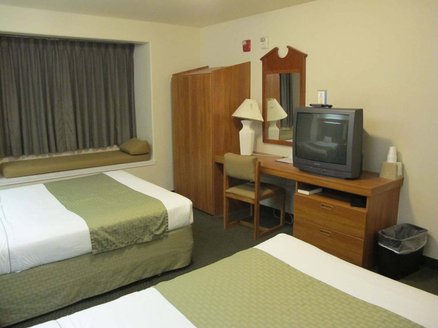 Ein Hotelzimmer mit zwei Betten, einem Schreibtisch mit Fernseher, einem Sessel, einer Lampe und einem Mülleimer.