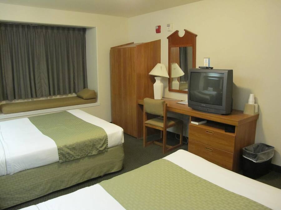 Ein Hotelzimmer mit zwei Betten, einem Schreibtisch mit Fernseher, einem Sessel, einer Lampe und einem Mülleimer.