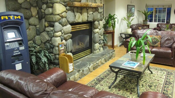 A living room with a stone fireplace, leather sofas, a coffee table, and an ATM machine. - Microtel Inn & Suites by Wyndham Eagle River/Anchorage Area (Eagle River)