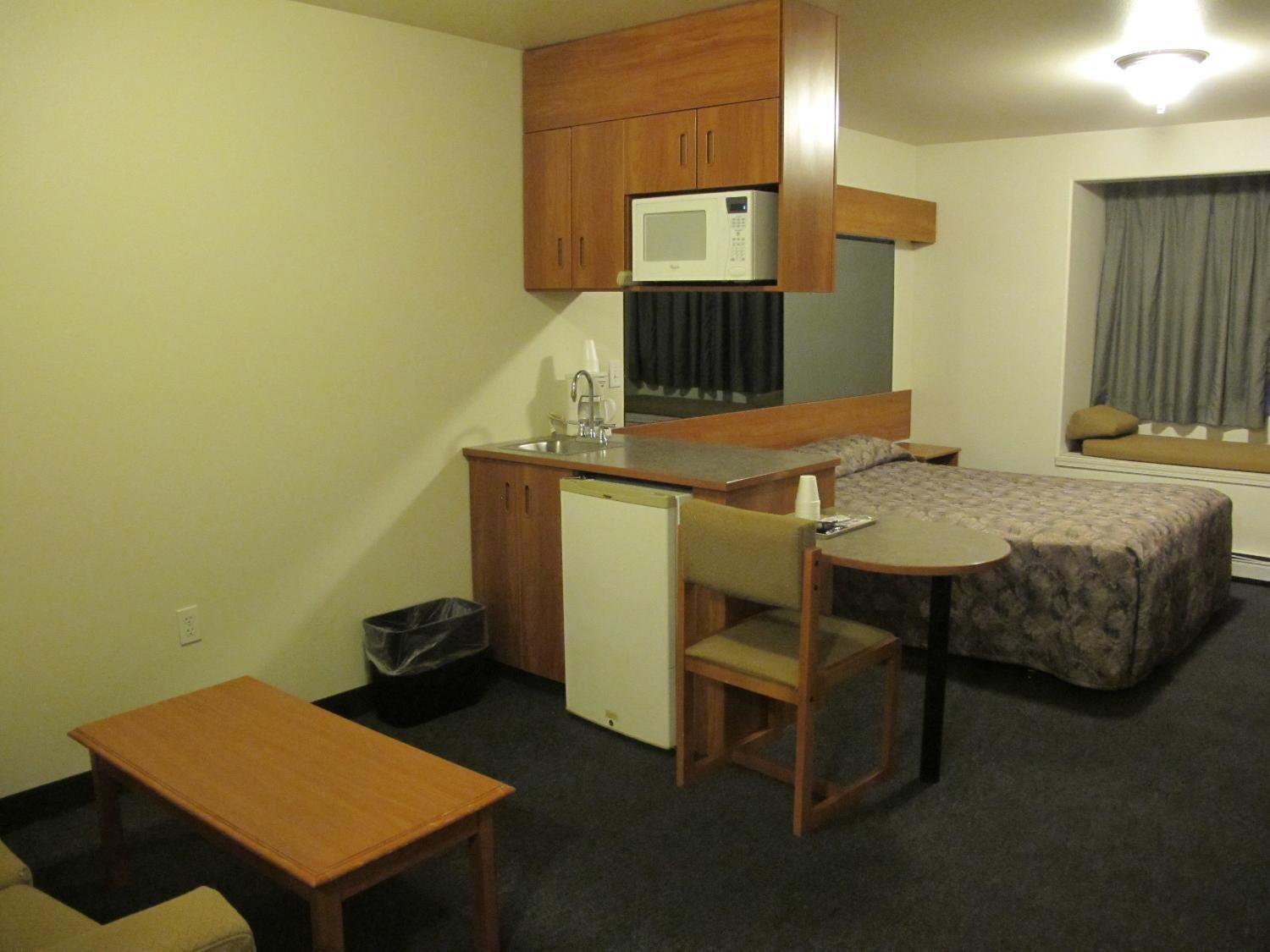Una habitación de hotel compacta con kitchenette, una cama individual, una mesita y una silla.