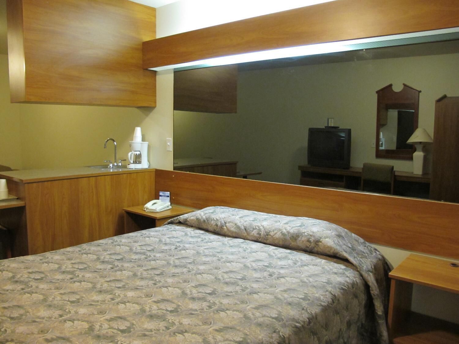 A hotel room with a bed, a bedside table, a desk with a telephone, a mirror, and a television.