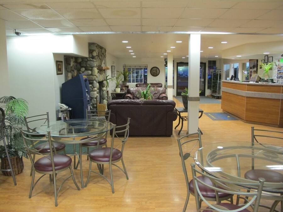 A spacious lobby with a stone wall, a reception desk, a brown leather sofa, and a glass table surrounded by chairs.