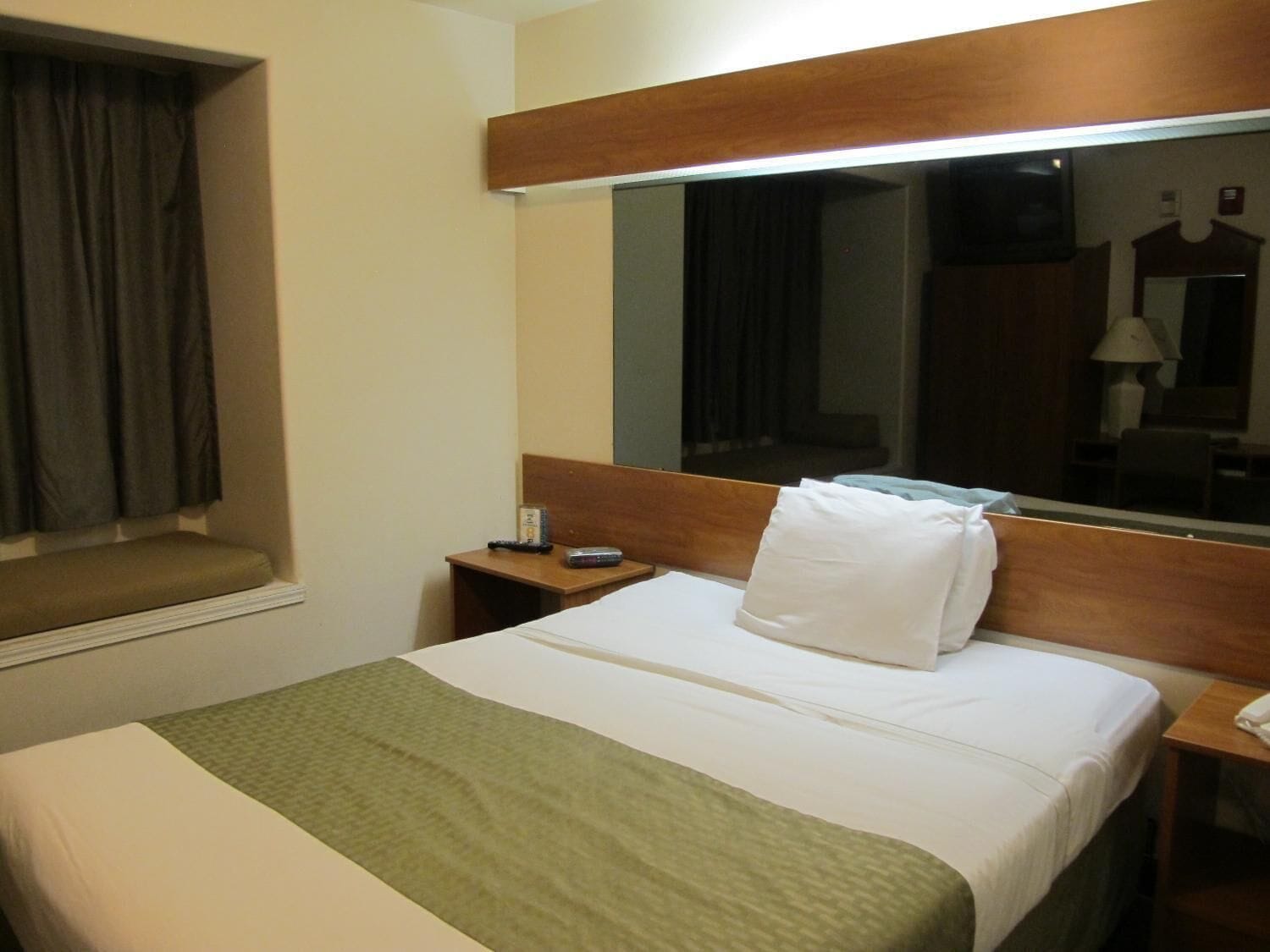 Ein Hotelzimmer mit Bett, Nachttisch, Spiegel und einem Fenster mit Vorhängen.