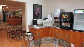 A modern kitchen area with a round glass table, metal chairs, a coffee machine, a microwave, and a refrigerator. - Microtel Inn & Suites by Wyndham Eagle River/Anchorage Area (Eagle River)