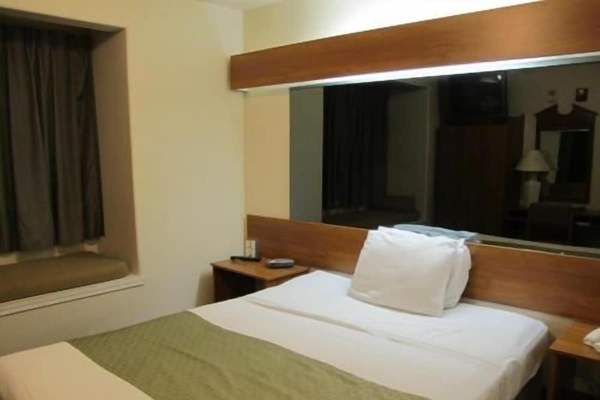 A hotel room with a bed, a nightstand, a mirror, and a window with curtains.