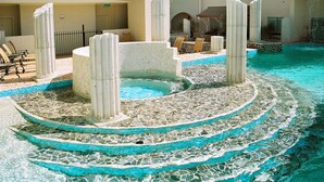 Zwembad met mozaïekpatroon, omringd door ligbedden en een kleine jacuzzi.