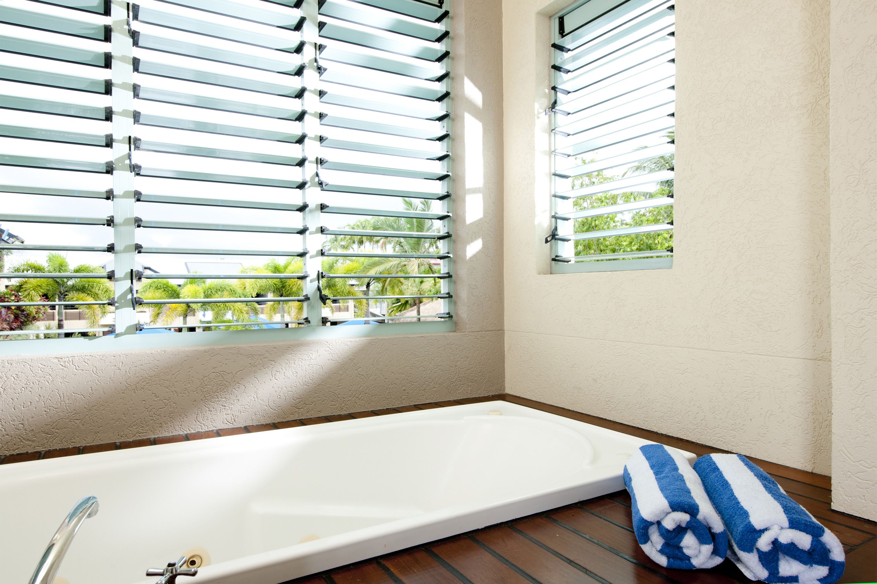 Un baño con bañera, una ventana con persianas y una toalla en el suelo.