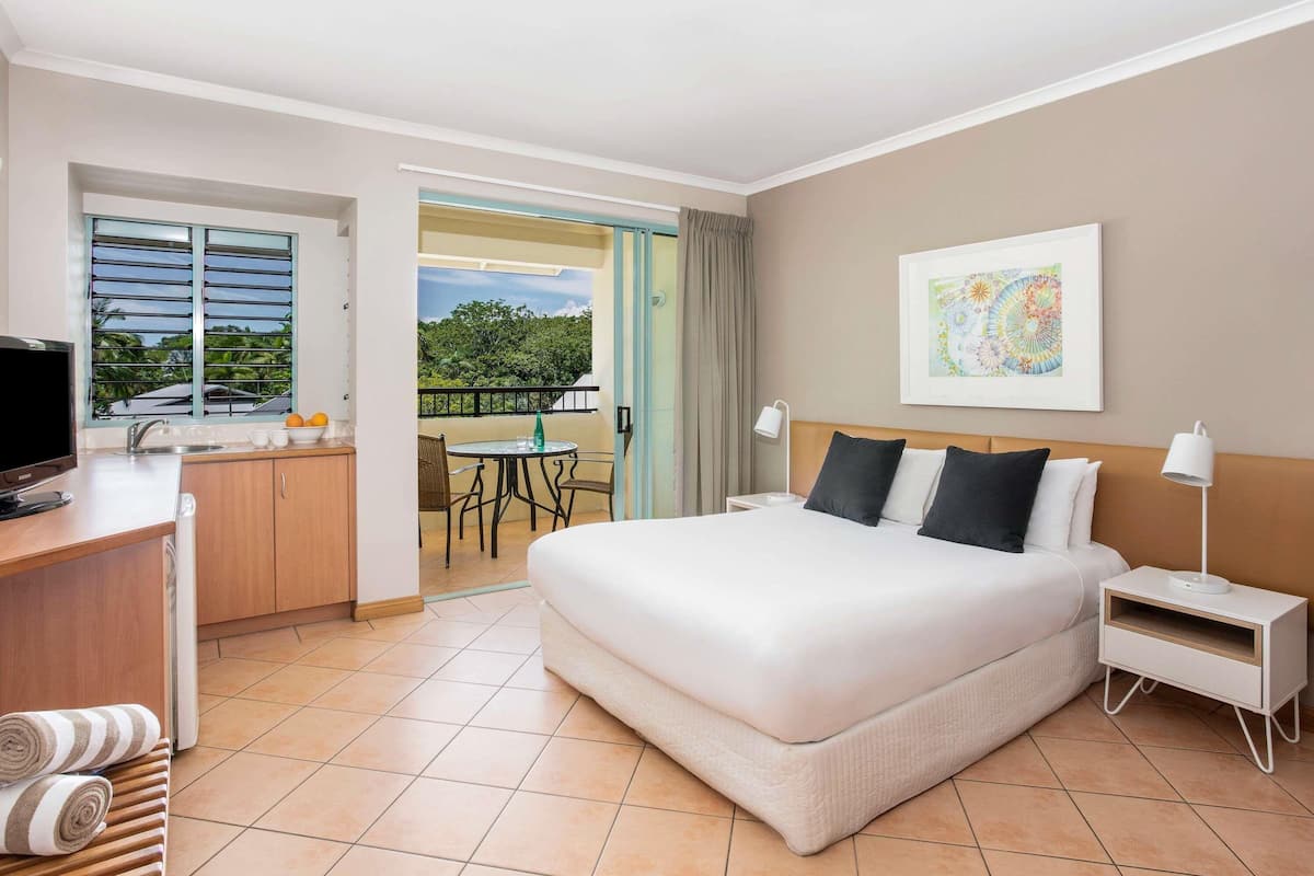 A hotel room with a bed, a desk with a TV, a balcony with a table and chairs, and a painting on the wall.