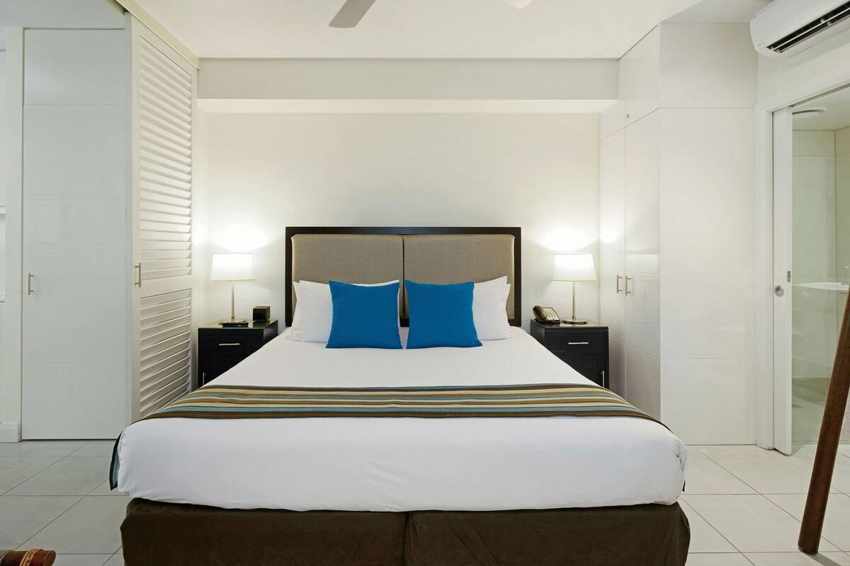 Une chambre d’hôtel avec un grand lit, deux tables de chevet, une armoire et une cabine de douche en verre.