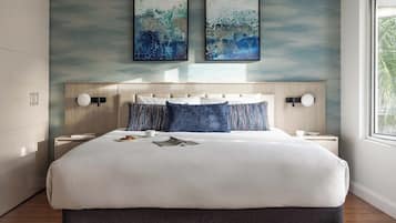 Una habitación de hotel moderna con una cama grande, dos mesitas de noche, un cabecero con iluminación integrada y dos obras de arte abstracto en la pared.