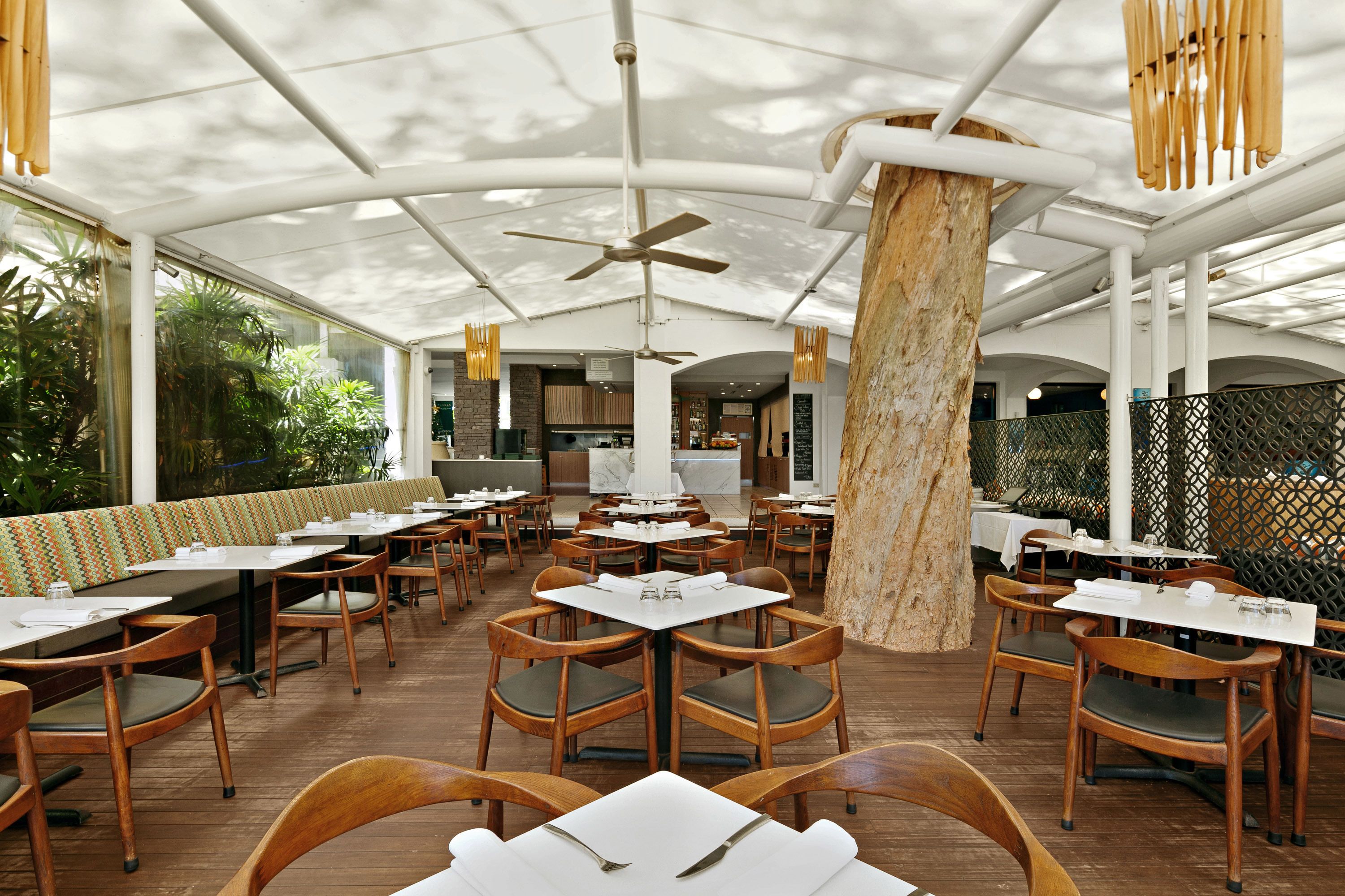 An indoor dining area with wooden tables and chairs, a central column, and a ceiling fan.