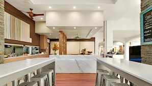 Una cocina moderna con una isla de mármol, taburetes de bar y un menú en una pizarra.