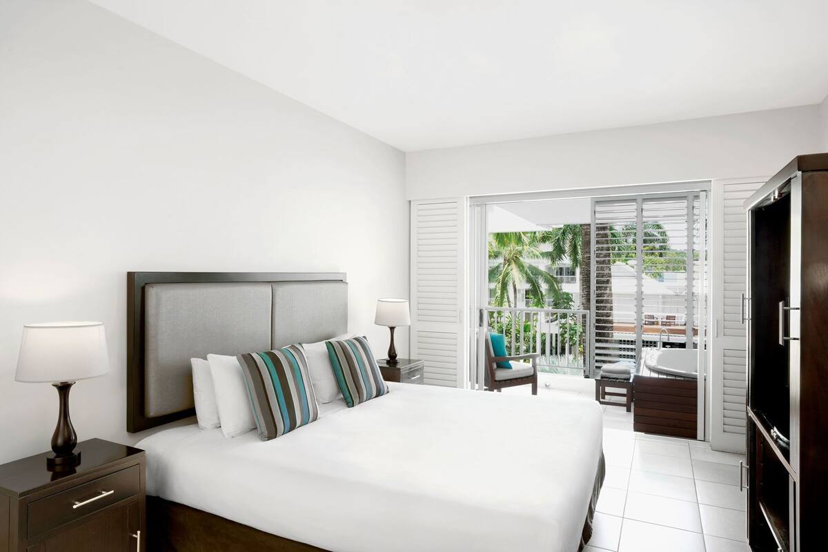 Une chambre d’hôtel avec un grand lit, une télévision, un bureau et un balcon offrant une vue sur les palmiers.