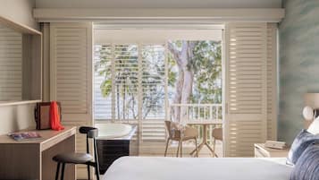 Habitación de hotel con cama, escritorio, silla, una computadora portátil y un balcón con vista a árboles.