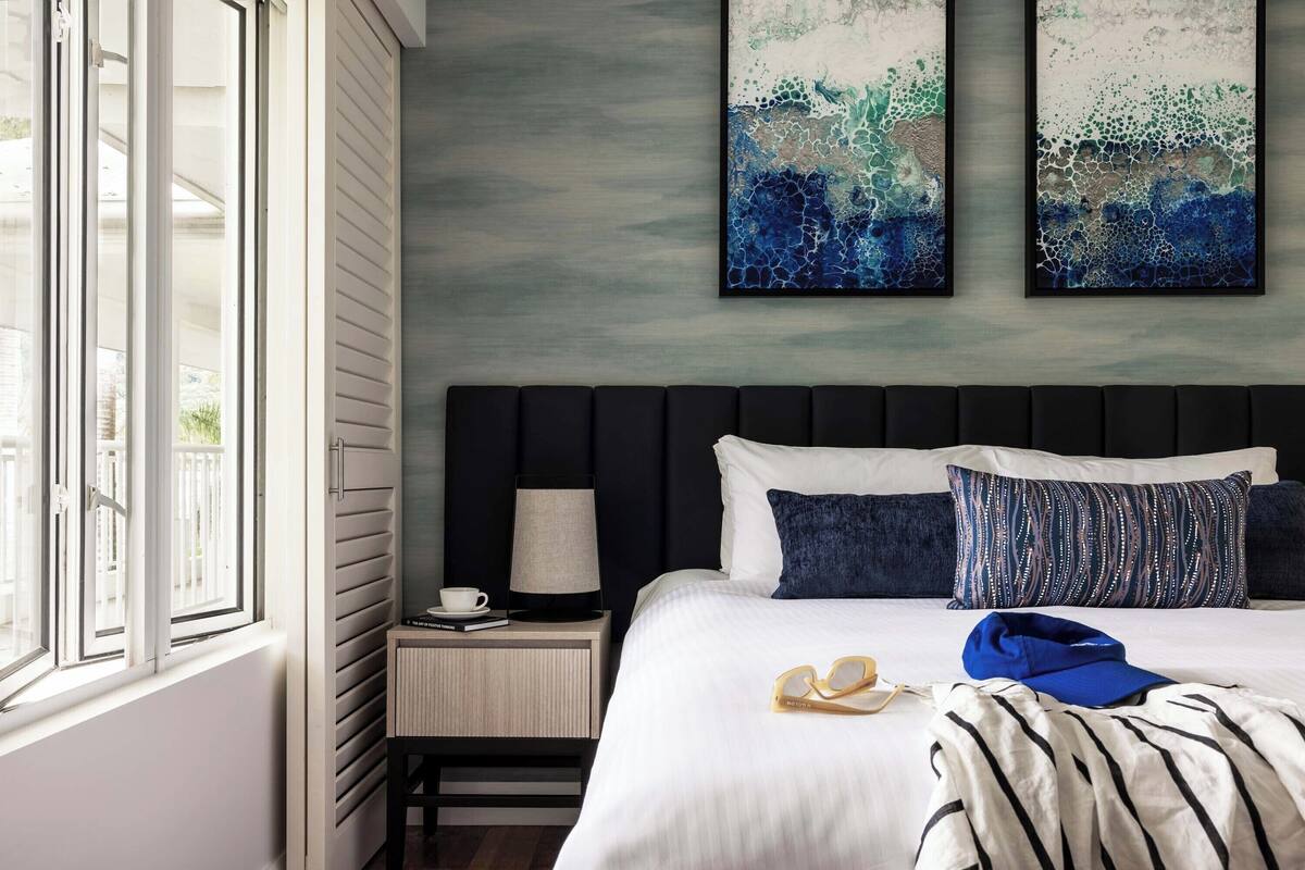 Une chambre d’hôtel avec un lit, une table de chevet, une lampe et deux tableaux abstraits accrochés au mur.