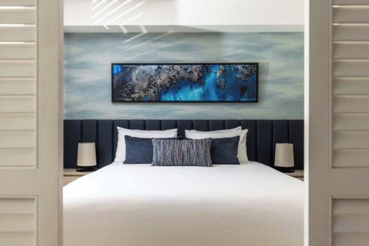 Una habitación de hotel moderna con una cama grande, un cabecero oscuro y un cuadro abstracto de gran tamaño sobre la cama.