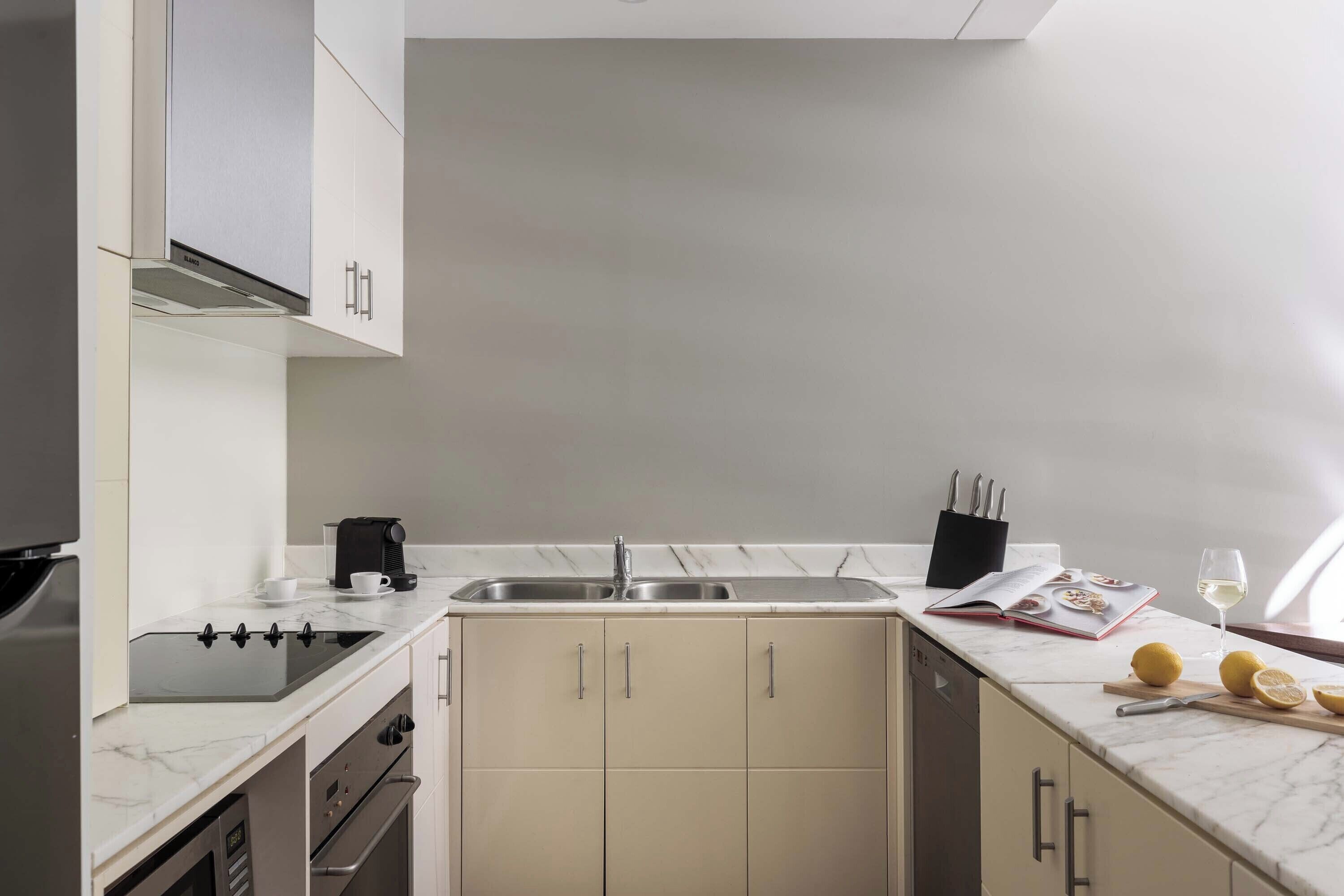 A modern kitchen with a built-in stove, a double sink, and a marble countertop.