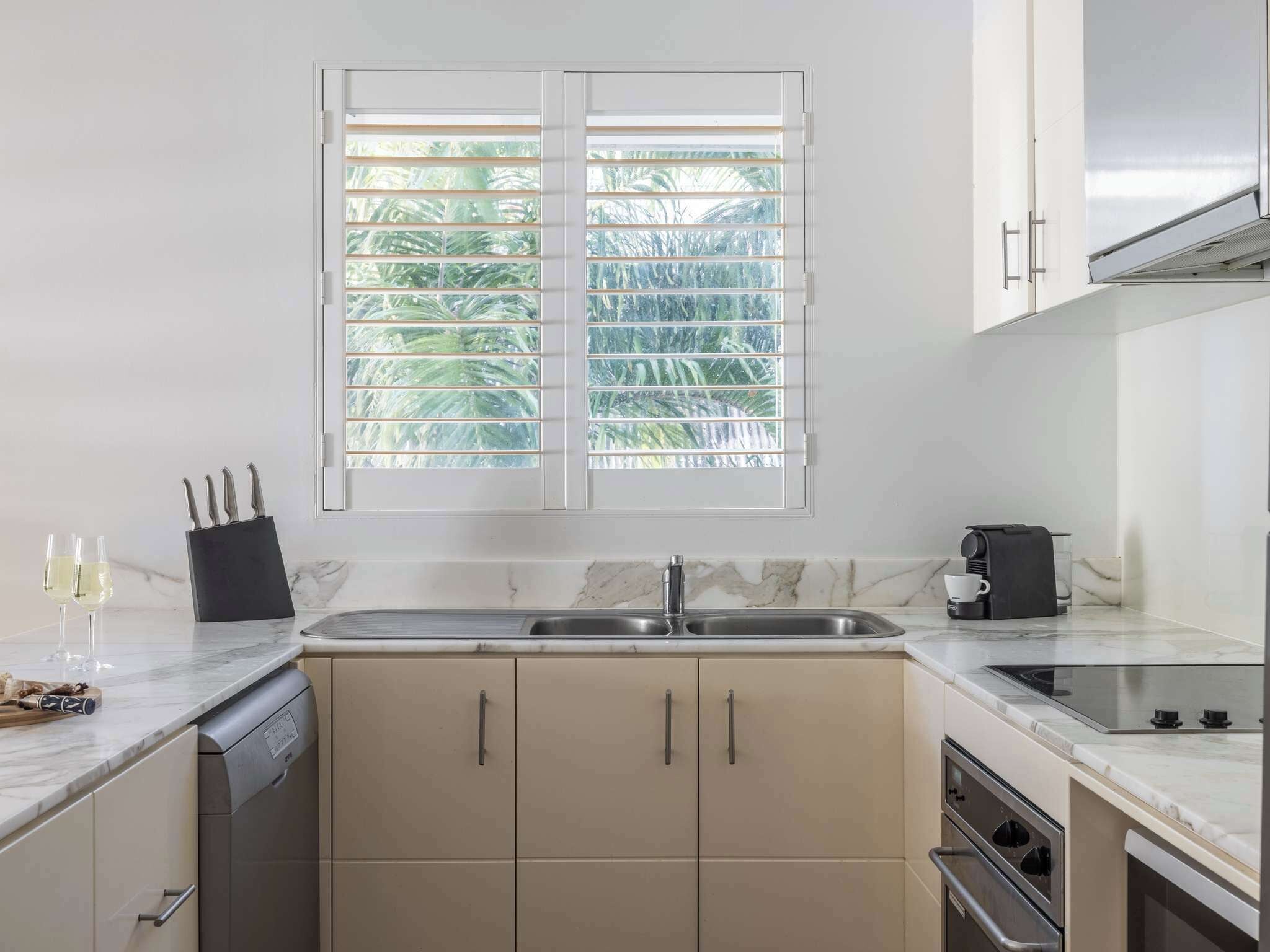 A modern kitchen with a double sink, a coffee maker, and a window with blinds.