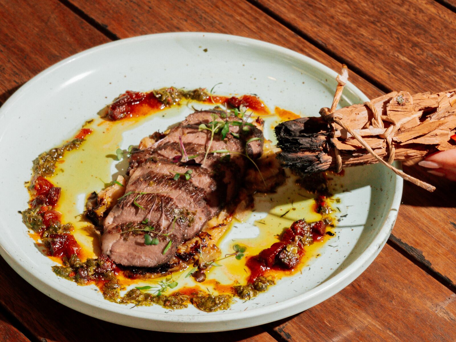 A plate with sliced meat, sauce, and herbs.