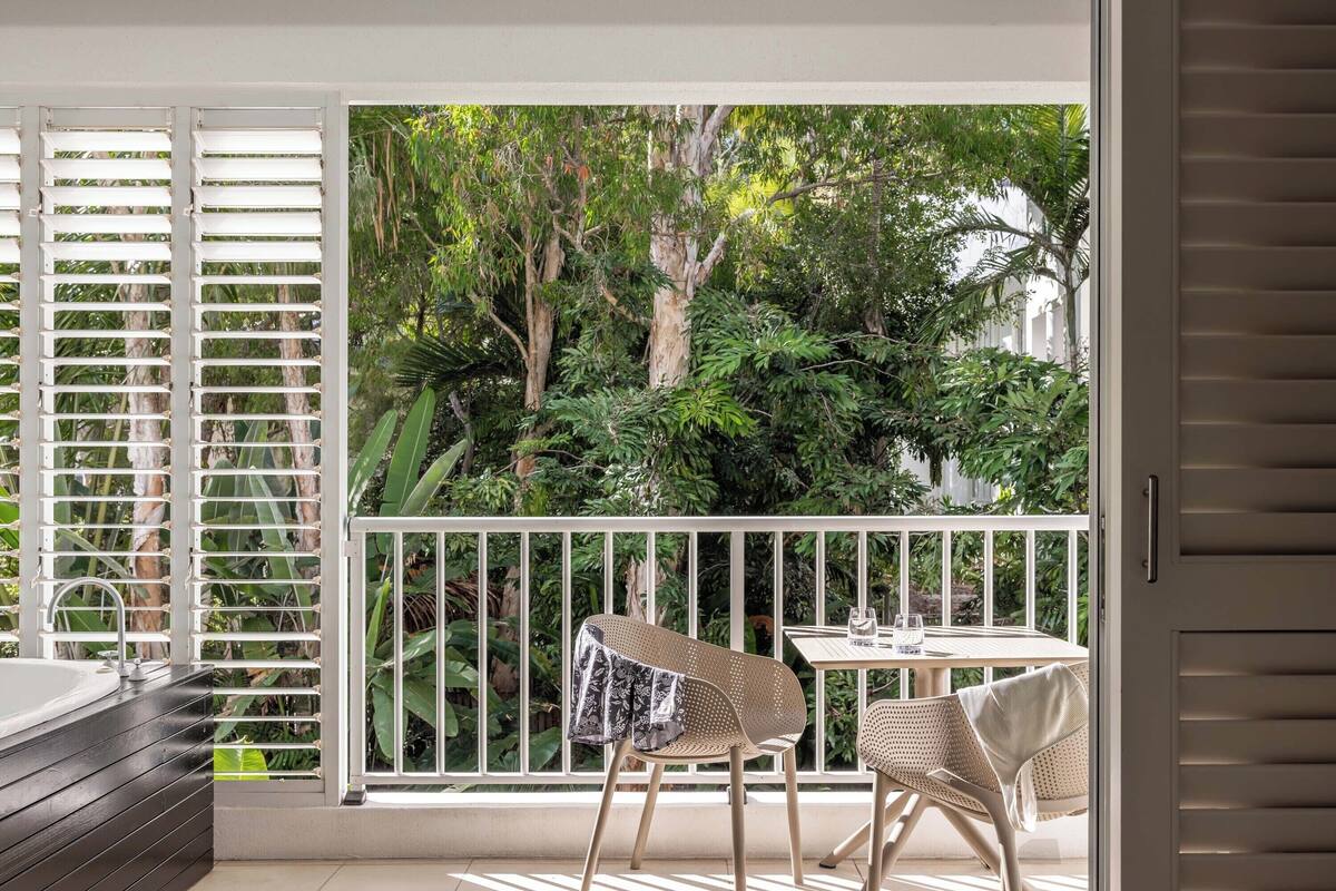 Un balcon doté d'une balustrade blanche, de deux fauteuils en osier, d'une petite table et offrant une vue sur une végétation luxuriante.