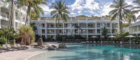 Un resort con piscina, palmeras y un edificio de varios pisos con balcones.