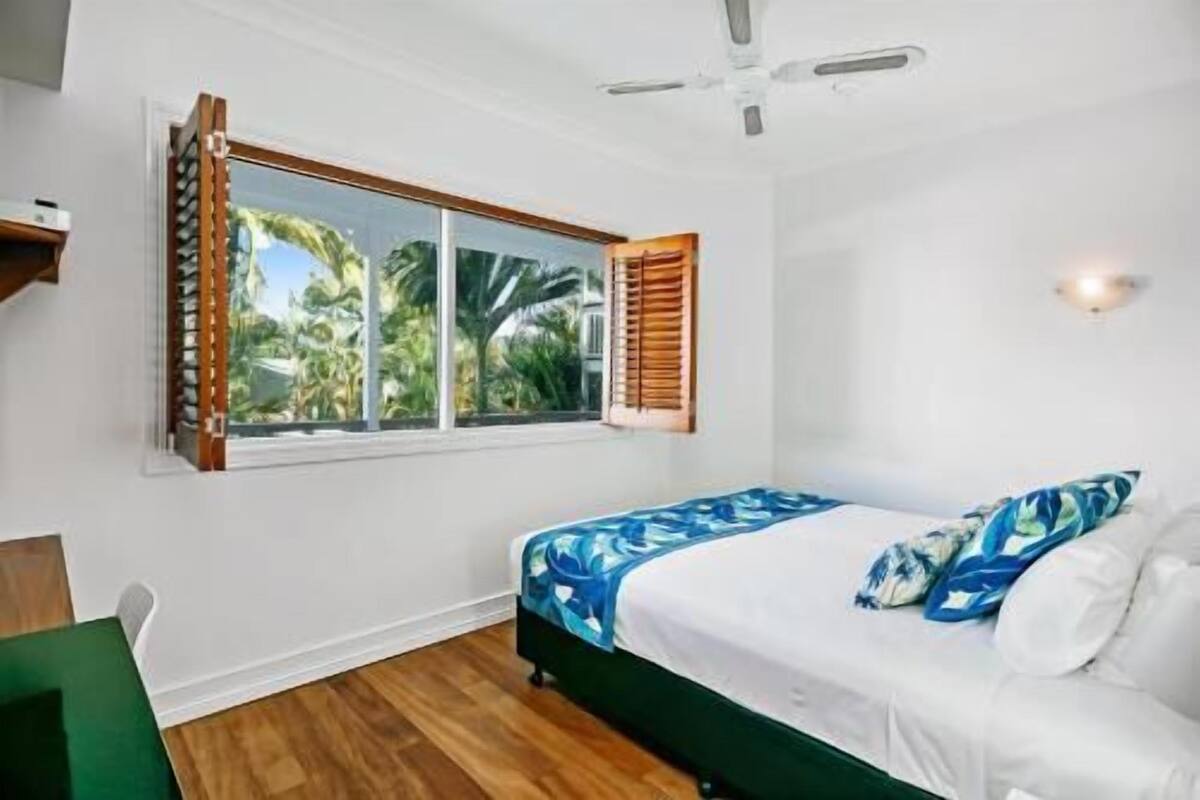 A bedroom with a bed, a window with blinds, a ceiling fan, and a wall-mounted light.