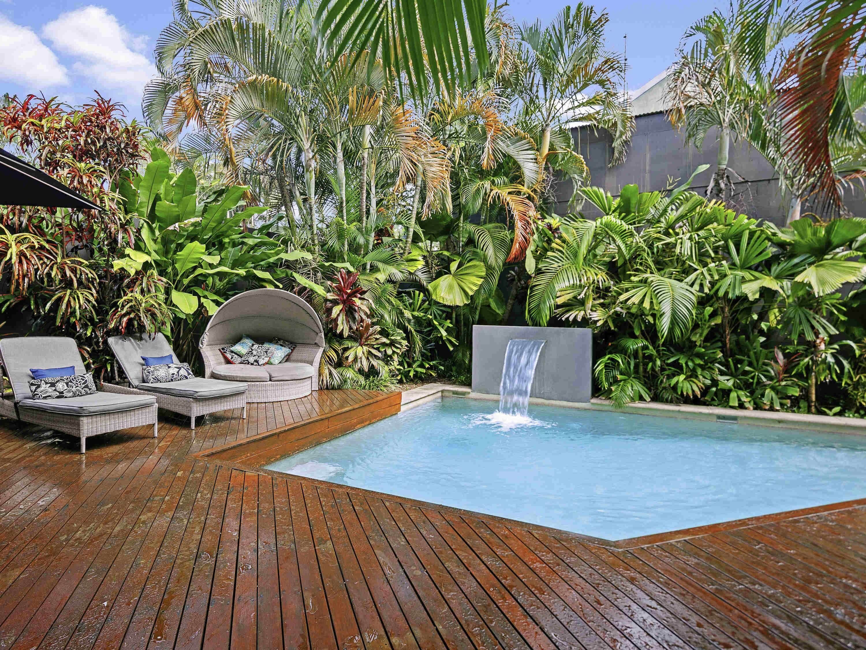A wooden deck with a pool, lounge chairs, and a waterfall feature.