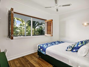 A bedroom with a bed, a window with shutters, a ceiling fan, and a view of palm trees. - Mantra On The Inlet (Port Douglas)