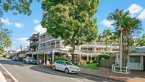 A street view with a white car parked on the side, storefronts, and a building with balconies.