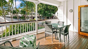 A covered outdoor area with a ceiling fan, a table with chairs, and a view of palm trees and buildings.