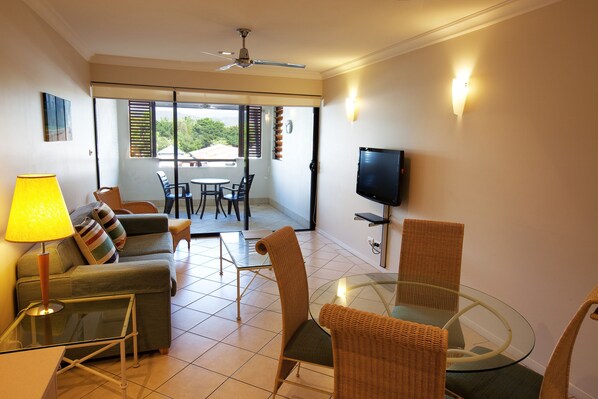 A living room with a sofa, chairs, a glass table, a TV, and a balcony with a view. - Mantra Heritage (Port Douglas)