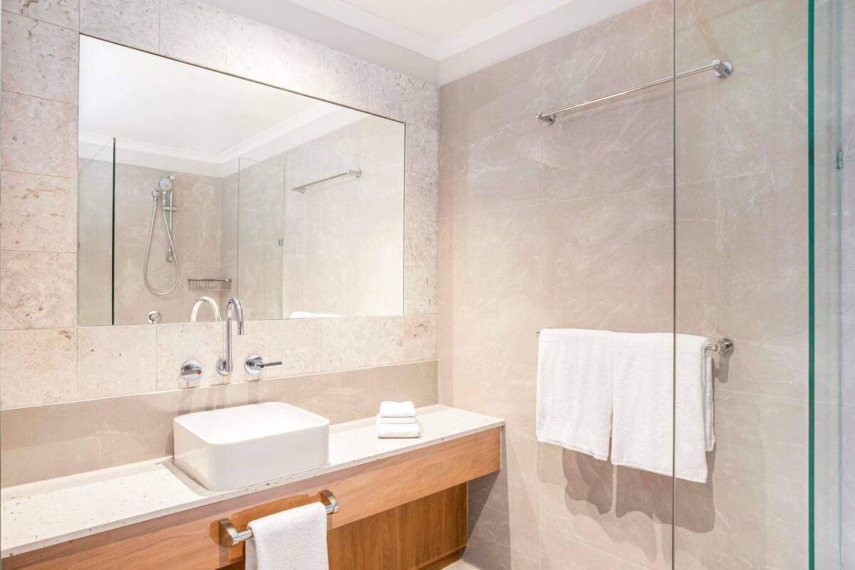 A modern bathroom with a large mirror, a sink, a shower, and a glass-enclosed shower area.