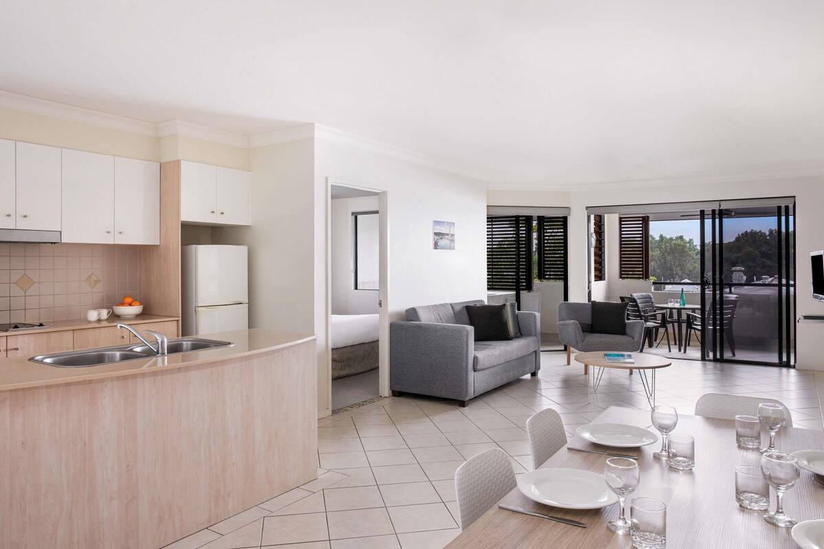 A modern kitchen with a sink, a dining area with a table set for four, and a living area with a sofa and chairs.