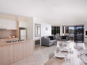 A modern kitchen with a sink, a dining area with a table set for four, and a living area with a sofa and chairs. - Mantra Heritage (Port Douglas)