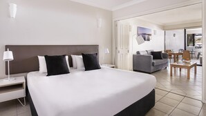 A hotel room with a large bed, a sofa, a dining table, and a view of the outside. - Mantra Heritage (Port Douglas)