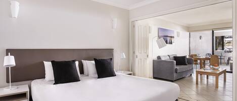 A hotel room with a large bed, a sofa, a dining table, and a view of the outside.