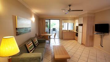 A compact living space with a sofa, a dining table, a kitchen area, and a TV mounted on the wall.