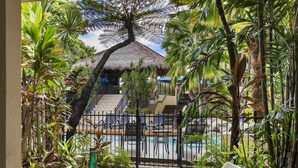 A tropical outdoor seating area with a pool, a thatched-roof structure, and lush greenery. - Mantra Heritage (Port Douglas)