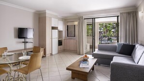 A modern hotel room with a dining area, a sofa, a TV, and a balcony with a view. - Mantra Heritage (Port Douglas)